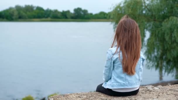 Μικρό κορίτσι που κάθεται στην όχθη του ποταμού. — Αρχείο Βίντεο