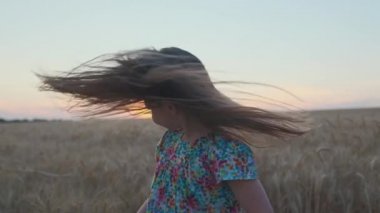 Küçük kız buğday tarlasında eğleniyor, oynuyor, saçlarını sallıyor. Yaz mutluluk havası. Sağlıklı bir yaşam tarzı. Gün batımında dışarıda eğlenmek. Doğa, bakım, dünya konseptini korumak