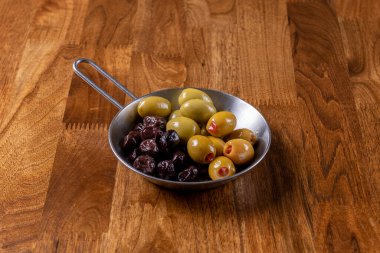 Ahşap arka planda bir tabakta farklı taze zeytin çeşitleri. Kapatın. Siyah ve yeşil zeytin.