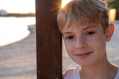 Çocuk kamerada gülümsüyor güneşli yaz gününün tadını çıkarıyor. Doğada, parkta ya da dışarıda genç bir çocuğun portresi. Mutlu aile kavramı veya başarılı evlat edinme veya ebeveynlik kavramı.