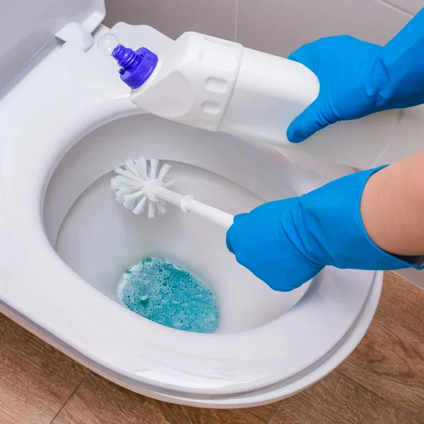 Clean toilet with cleaner and a whitening gel with a gloved hand and brush. The concept of the home cleaning, cleaning service