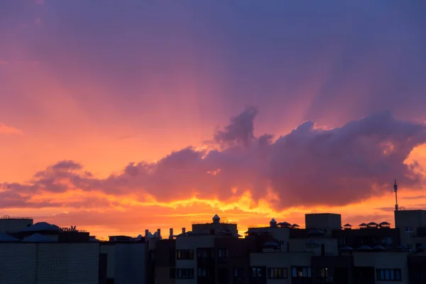 Pink orange purple sunset over the city. Multicolored sky and black silhouette of tall buildings of the metropolis. Big cloud and sun rays