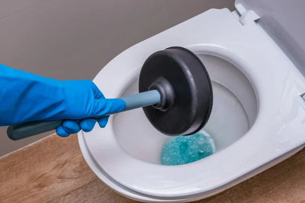 A clean toilet with cleaning agent and a gloved hand with a plunger. The concept of the home cleaning, cleaning service