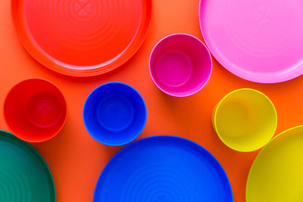 Children's unbreakable multicolored dishes, serving for a children's holiday. Isolated on an orange background