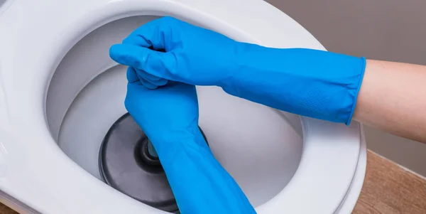 A clean toilet with cleaning agent and a gloved hand with a plunger. The concept of the home cleaning, cleaning service