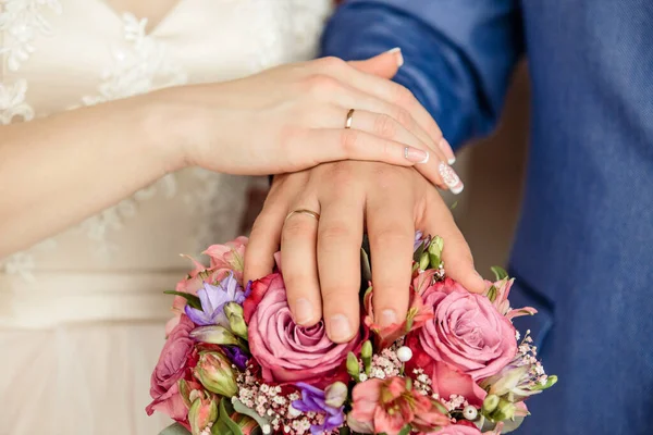 Hands of the bride and groom with rings, folded on a bouquet — Stock Photo, Image