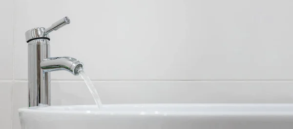 Wasser fließt aus dem Wasserhahn im Badezimmer. Chrom Sanitär-und Keramik-Waschbecken Fliesen Hintergrund lizenzfreie Stockbilder