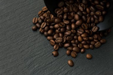 Bir fincanda bir sürü kahve çekirdeği, kayrak taşının siyah desenli arka planında. Metin için alanı kopyala