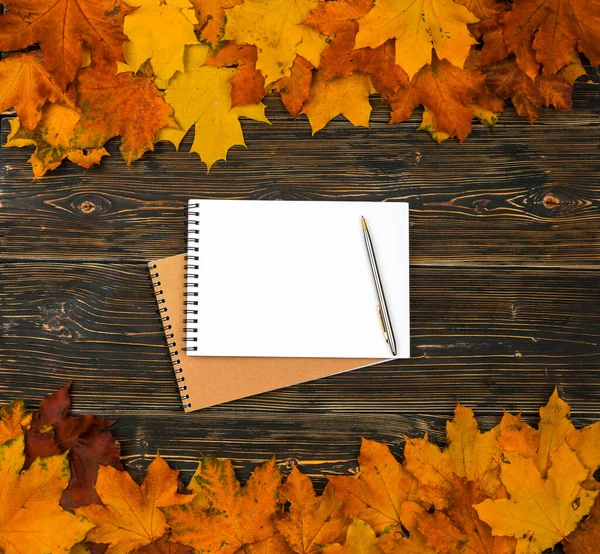Karanlık bir ahşap masaya karşı parlak bir sonbahar yaprakları yığını üzerinde metin için boş bir yeri olan bir defter.