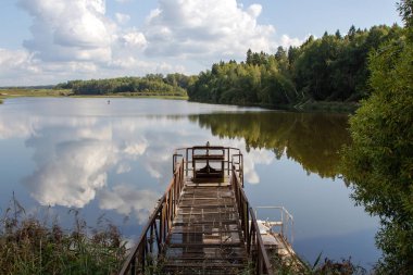 Bulutlar nehre yansıyor. Güzel nehir manzarası. Küçük bir teknolojik köprü, su deşarjı için bir cihaz. Güzel nehir manzarası. Bulutların sudaki yansıması. Suyun yüzeyi