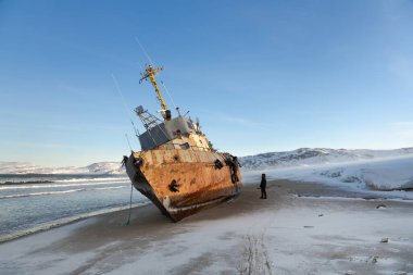 Yan yatmış bir balıkçı teknesi, Barents Denizi kıyısında bir fırtınayla karaya vurmuş, Kola Yarımadası, Teriberka, Rusya