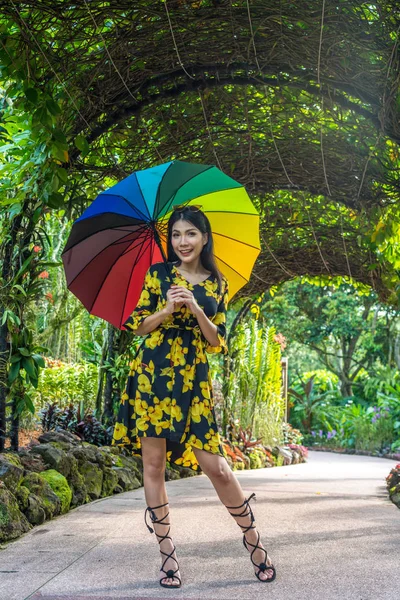迷人的美丽的亚洲女士长黑发拿着彩虹多色伞看相机在户外公园花园 — 图库照片