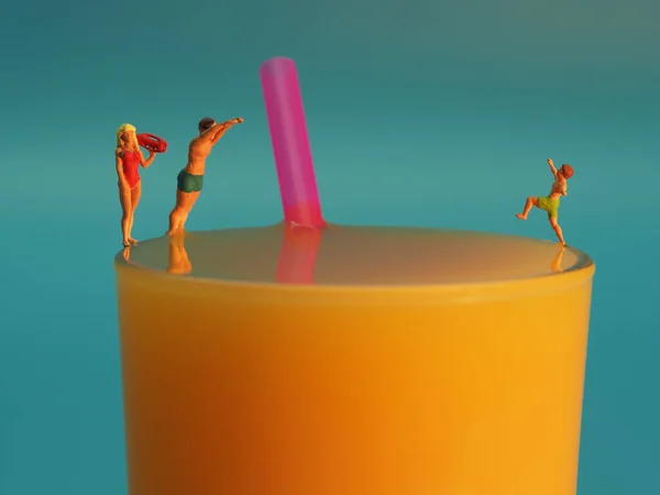 Glas Orangensaft mit Strohhalm und drei Miniatürfiguren