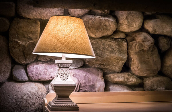 Каменная стена со стильной лампой на деревянном столе
