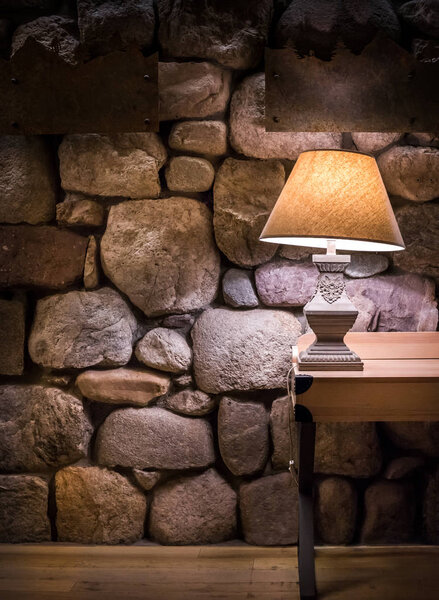 Каменная стена со стильной лампой на деревянном столе

