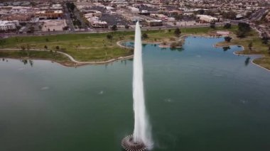 Şehir parkının ortasında küçük bir göl de gökyüzünde yüksek su püskürtme büyük uzun çeşme Çarpıcı hava drone 4k atış