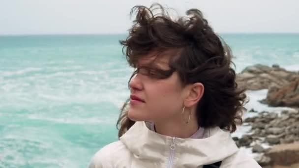 Jonge vrouw met krullend haar zwaaiende op de wind tegen een ongericht uitzicht op zee — Stockvideo