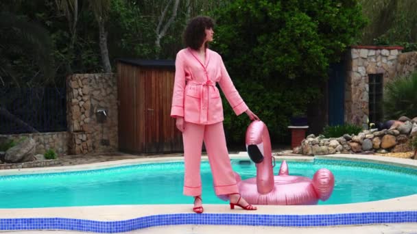 Mladá modelka v růžovém pyžamu nedaleko bazénu, dotýkala se růžového plameňáka — Stock video
