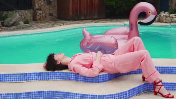 Красива жіноча модель в рожевих ПДж позує біля басейну з рожевим гумовим кільцем — стокове відео