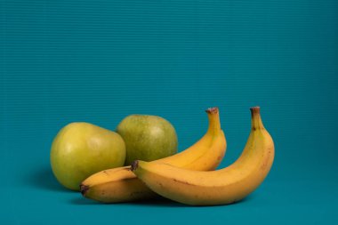 Açık mavi bir arka plan üzerinde iki muz ve iki yeşil elma