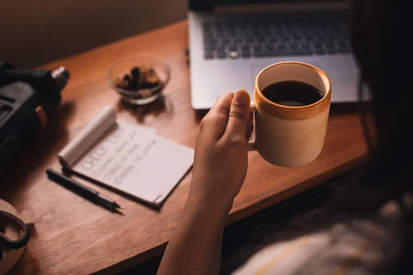 Bir kadının eli, bir fincan kahve, fındık, angarya bir liste, bir dizüstü bilgisayar ve aletlerle ev eşyaları hazırlıyor.