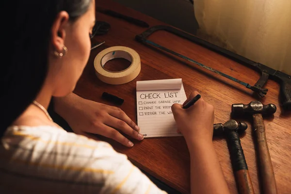 Bir kadın ahşap bir masada el aletleri ile ev işleri listesi yapıyor.