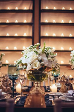 Gözlüklü Noel masası, çatal bıçak takımı, mumlar ve beyaz çiçekli cam vazo.