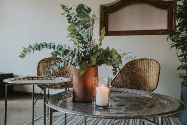 Hasır sandalyeli metal masa, ahşap vazolar, halı ve ayna.