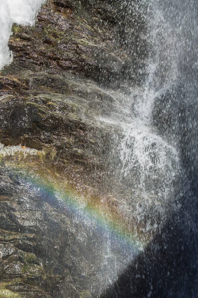 Water stroomt over een met mos bedekte rots maakt een regenboog verschijnen. — Stockfoto