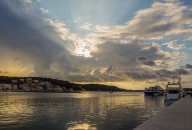 Bir yelkenli dramatik bulutların arkasında akşam güneşinde iskelede yatlar geçer.