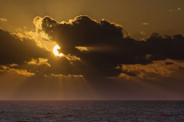 Batan güneş, mor bir Karayip Denizi üzerinde bulutların arkasına saklanıyor.