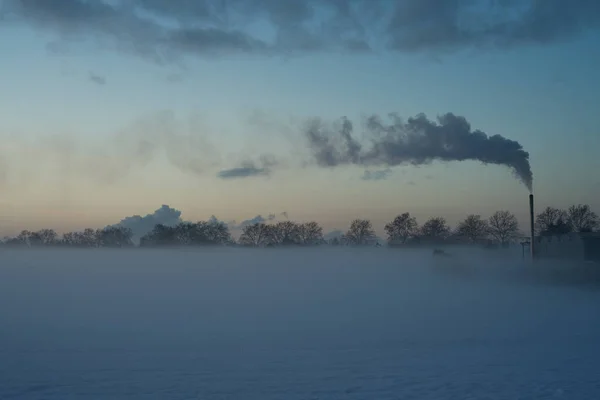 Sunset on a very cold winter day, with a smoking chimney. — Stock Photo, Image