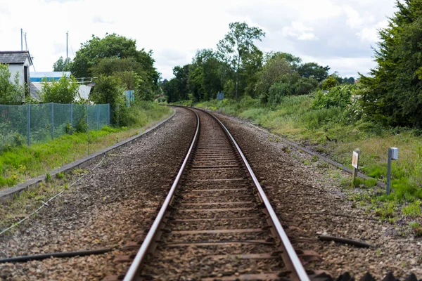 Un único conjunto de vías de tren que conducen a un punto de fuga en el horizonte, la línea de tren está atravesando el campo rural británico —  Fotos de Stock