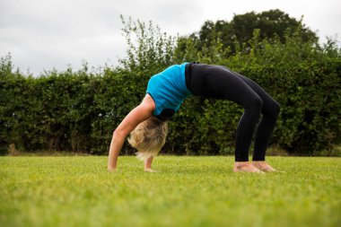 Çimenli bir parkta çıplak ayak yoga yapan orta yaşlı bir kadın.
