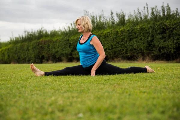 A middle aged woman practicing yoga barefoot outside in a grassy park