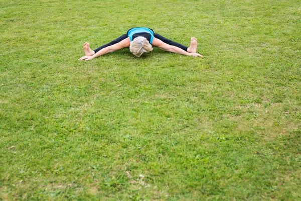 Uma mulher de meia-idade praticando ioga descalça lá fora em um parque gramado — Fotografia de Stock