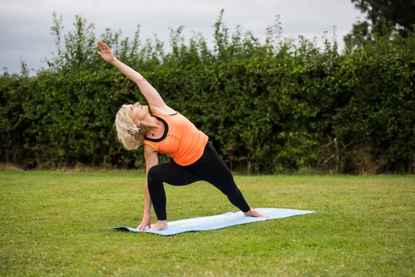 Çimenli bir parkta çıplak ayak yoga yapan orta yaşlı bir kadın.