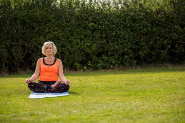 Çimenli bir parkta çıplak ayak yoga yapan orta yaşlı bir kadın.