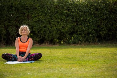 Çimenli bir parkta çıplak ayak yoga yapan orta yaşlı bir kadın.