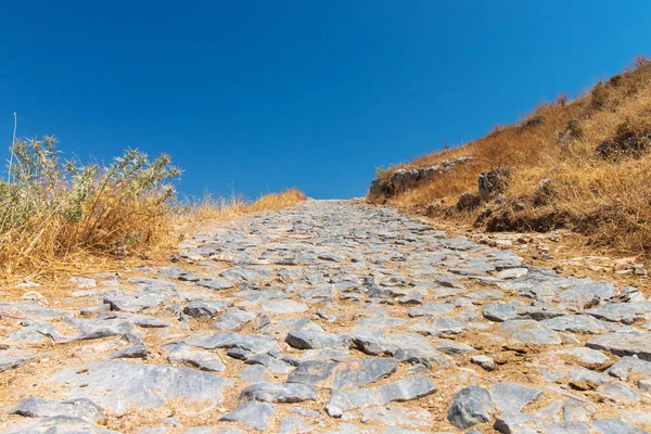 Lonely path of stones with dried out vegetation on the roadside in Rhodes, Greece — Stock Photo, Image