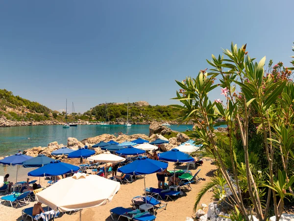 Rodos, Yunanistan - 5 Temmuz 2019 - Güzel Rodos adasındaki bir körfezde, tatilciler şemsiyeler altında dinleniyorlar
