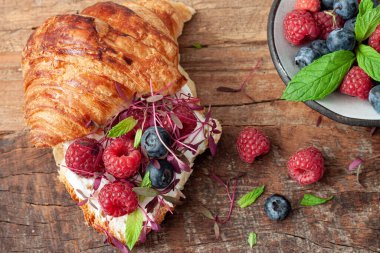 Taze kruvasanlarla nefis kahvaltı ve ahşap arka planda olgun böğürtlenler.