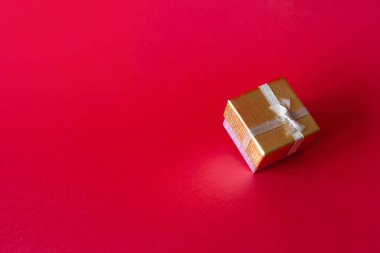 Kırmızı arka plan üzerinde bir altın hediye kutusu.