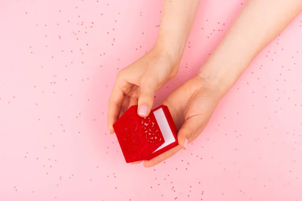 Chica abre una caja de regalo de terciopelo rojo sobre un fondo rosa Imagen De Stock