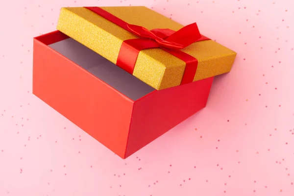 Red gift box with a gold lid with a bow on a pink background. — Stock Photo, Image