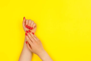 Sarı arka planda kırmızı manikürlü kadın elleri. Üst görünüm.