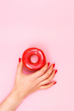 Mükemmel manikürlü güzel bir kadın eli pembe arka planda kırmızı çöreği tutar..