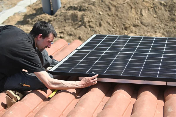 Building worker installing solar panel on roof of individual house