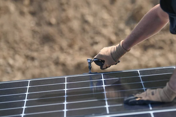 Building worker installing solar panel with screwdriver on roof of individual house