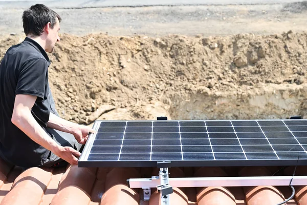 Building worker installing alternative energy photovoltaic solar panels on roof of individual house